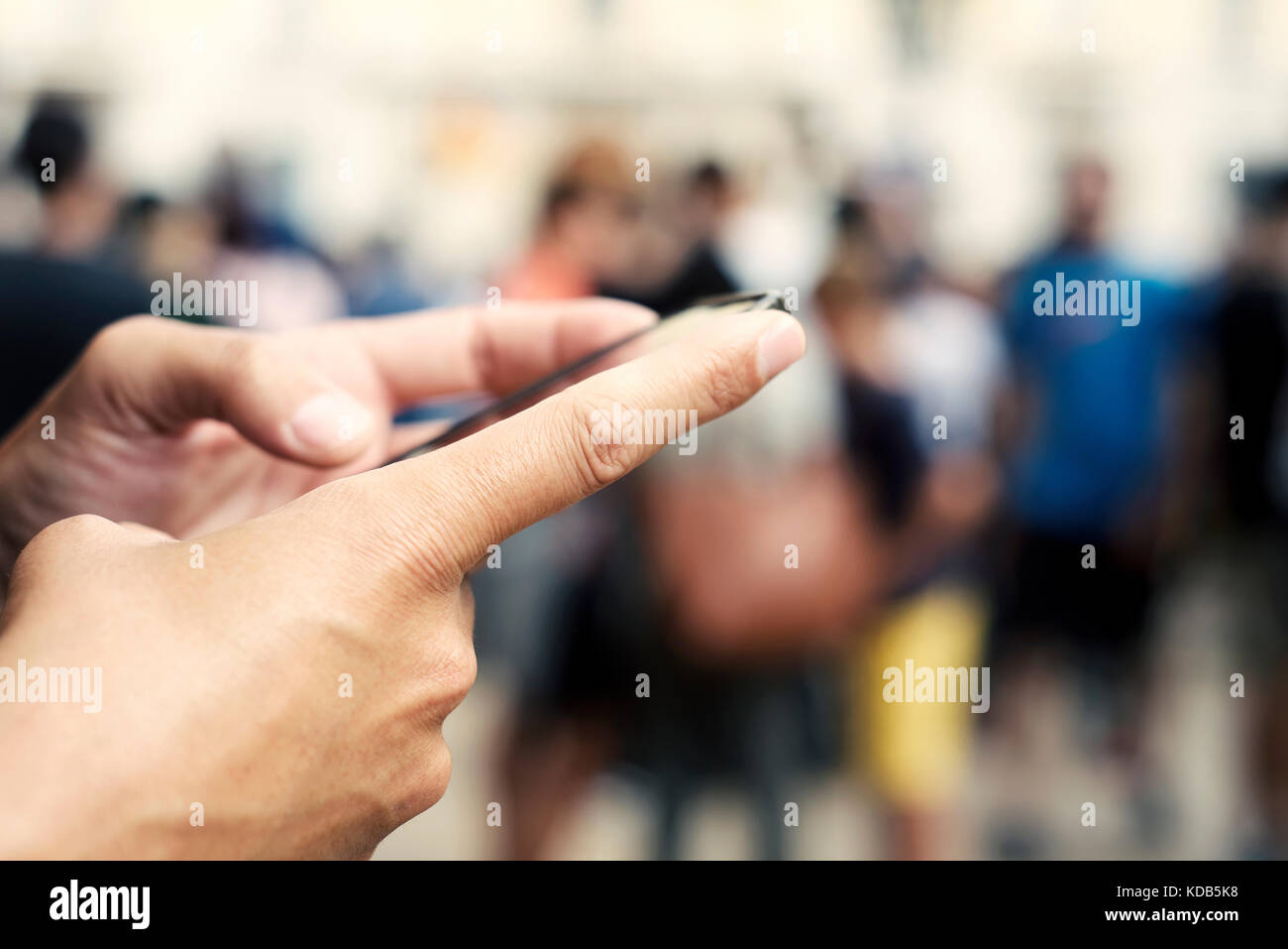 closeup of a young caucasian man using a smartphone in the street, with unrecognizable people in the background Stock Photo