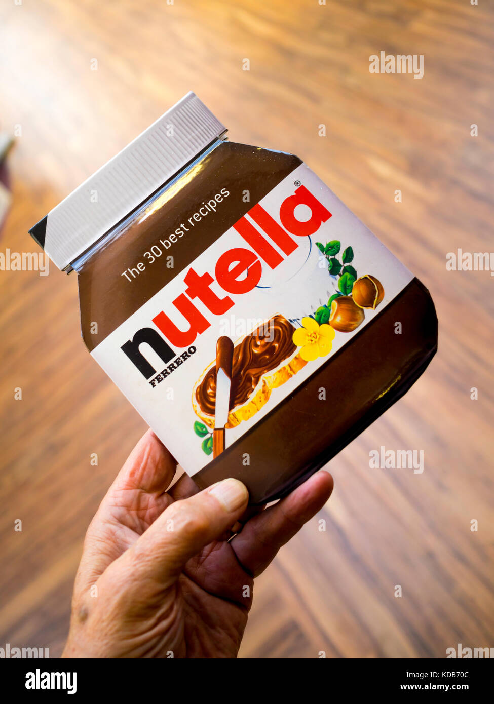 A man's hand holding a cookery book shaped like a jar of Nut paste Nutella and providing 30 best recipes for its use Stock Photo