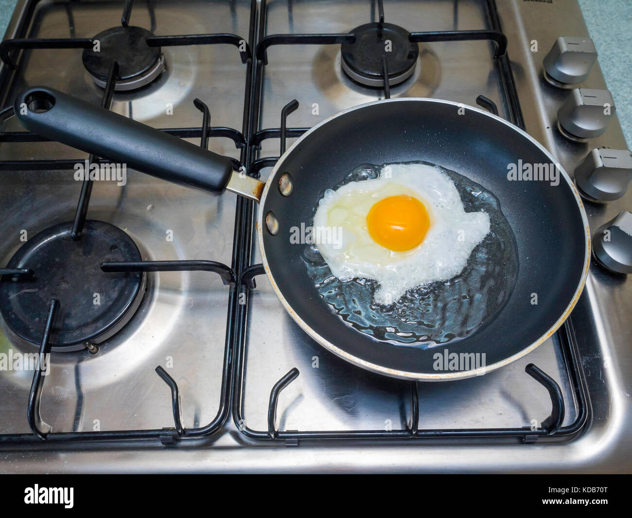 An egg being fried in sunflower oil in a small Teflon coated non stick frying pan on a gas hob Stock Photo