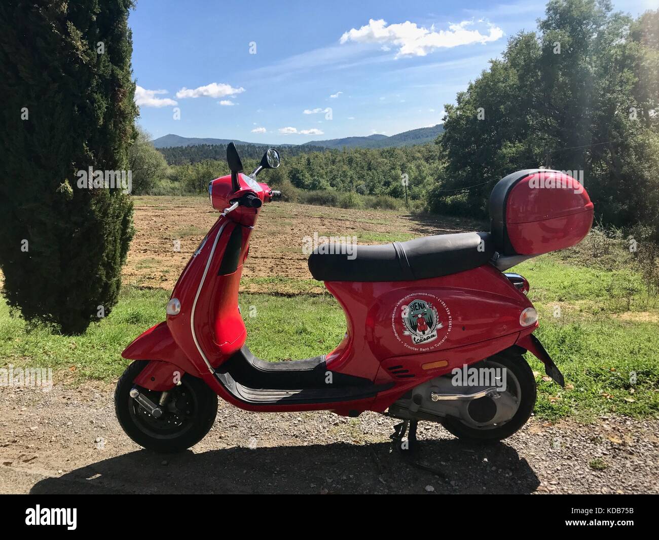 San Galgano, Italy - September 25, 2017: A red color vintage scooter for rent by Siena Vespa is parked in beautiful Tuscan landscape Stock Photo