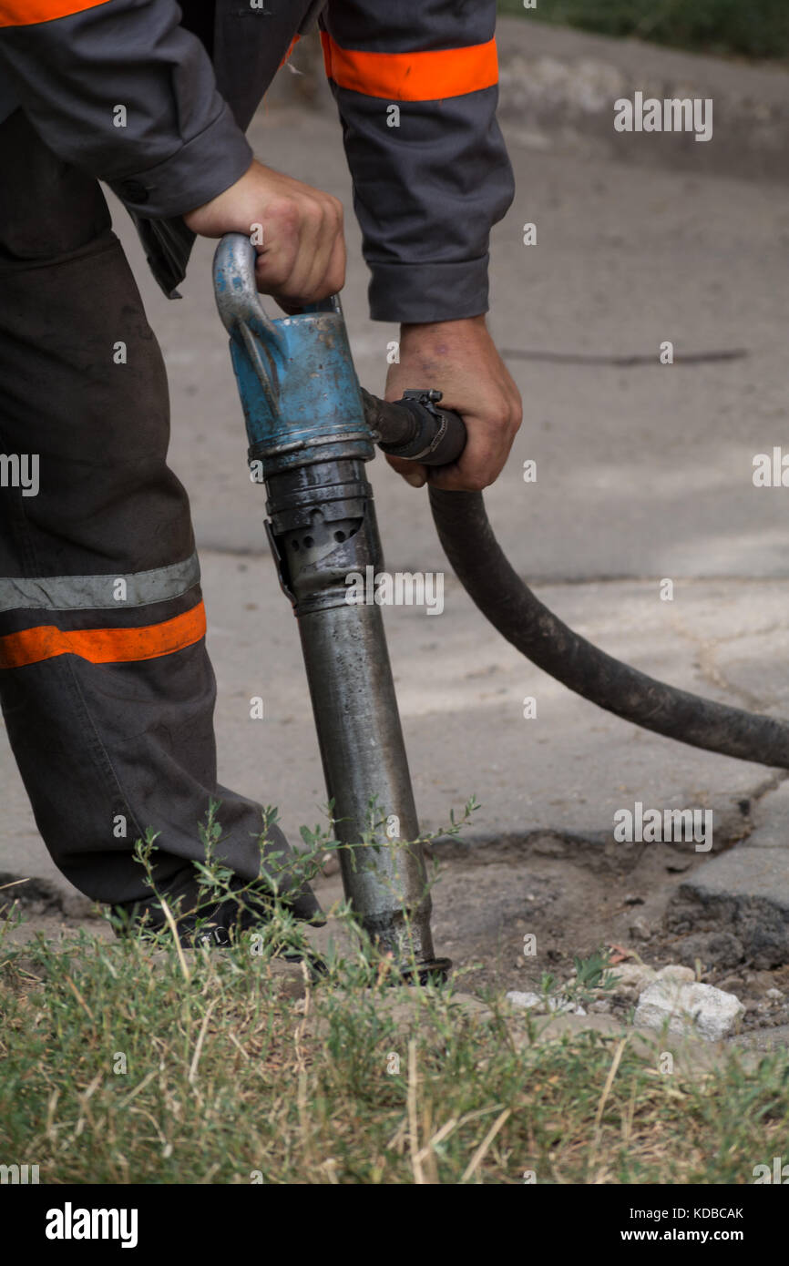 Road repairing works with jackhammer. Male worker using jackhammer