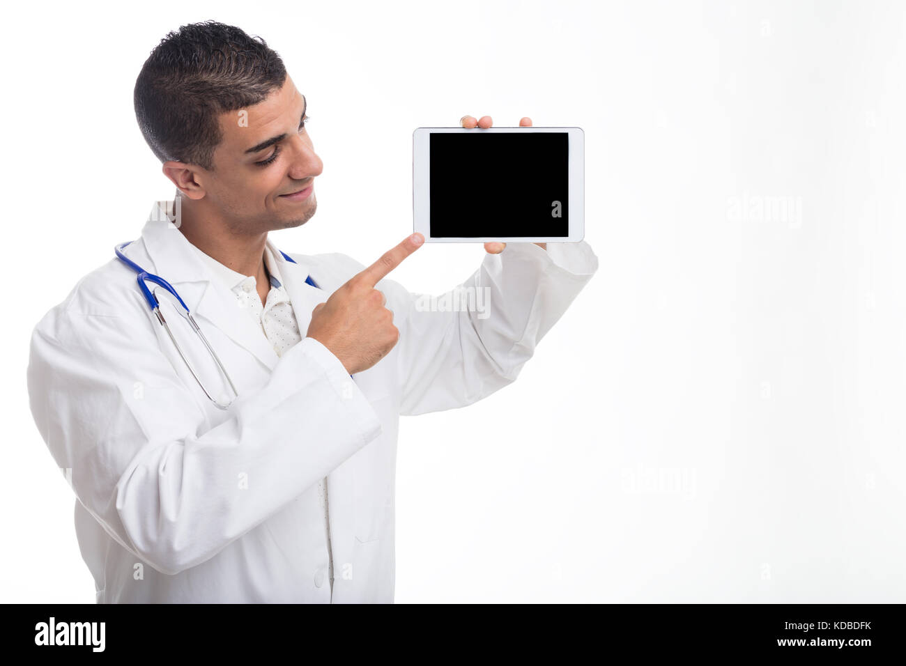 Young smiling man wearing white gown pointing at digital tablet against white background Stock Photo