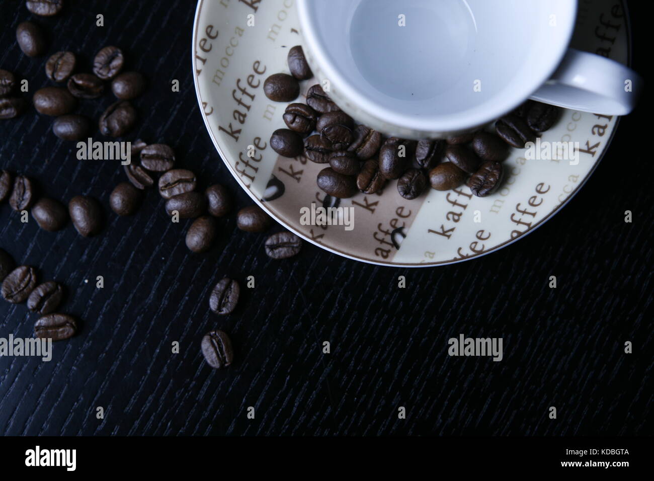 Moccatasse kaffeetasse mit verstreuten Kaffee Bohnen auf schwarzem tisch - Mocca cup coffee cup with scattered coffee beans on black table Stock Photo