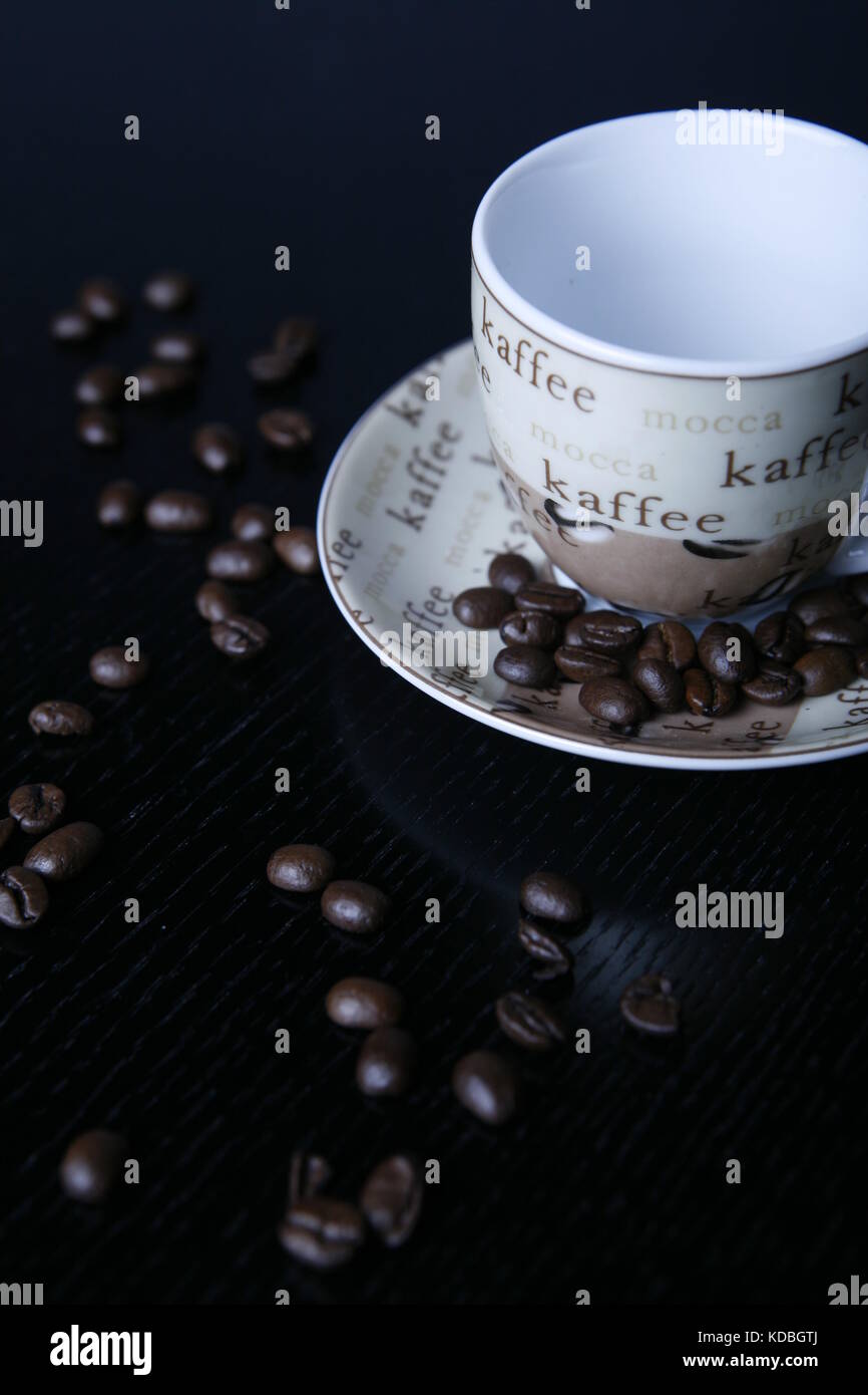 Moccatasse kaffeetasse mit verstreuten Kaffee Bohnen auf schwarzem tisch - Mocca cup coffee cup with scattered coffee beans on black table Stock Photo