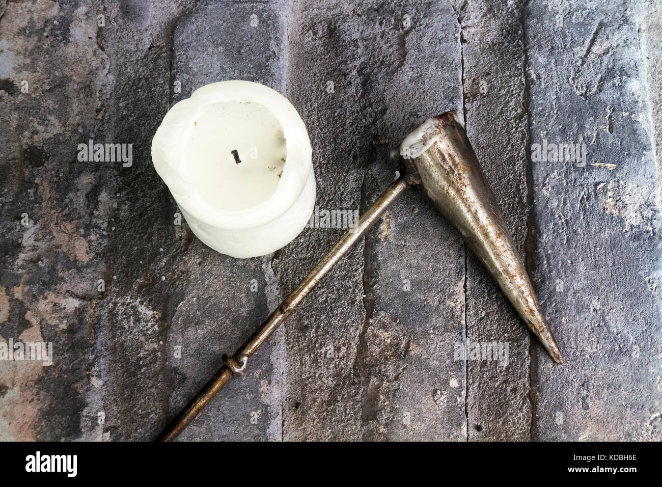 White church candle with a metal candle snuffer on a stone background