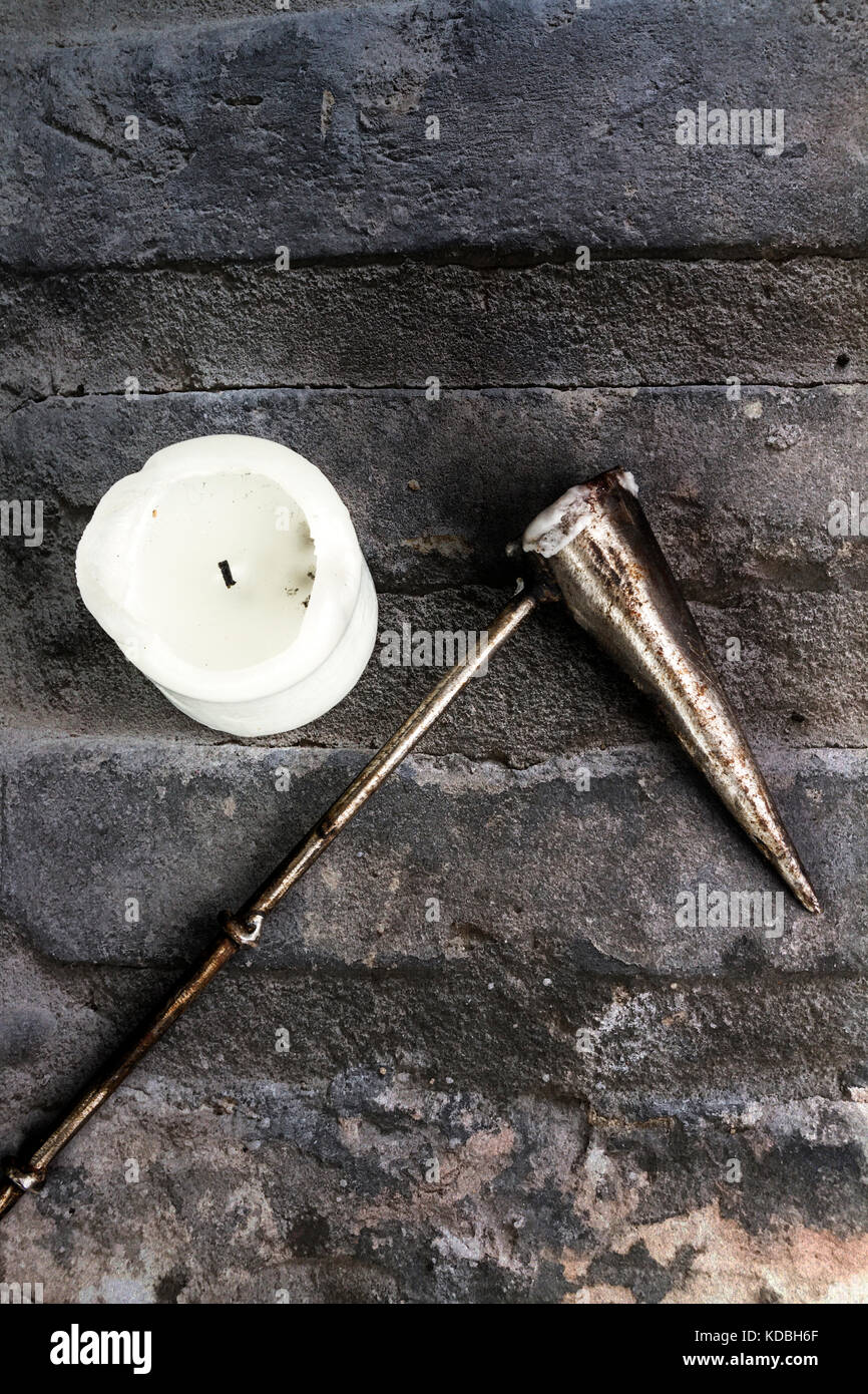 White church candle with a metal candle snuffer on a stone background