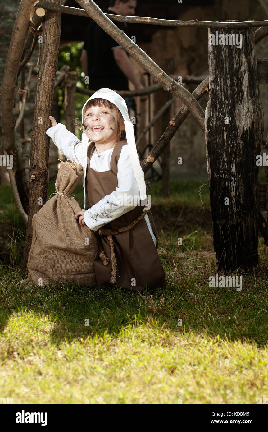 Smiling medieval style girl have sitting on the grass neare a sack Stock Photo
