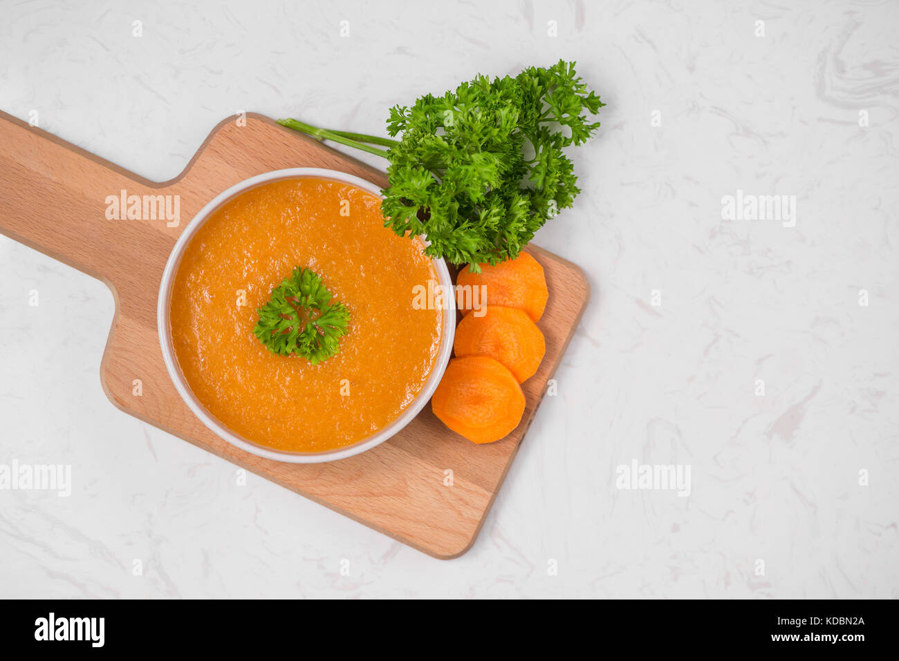 Carrot soup with cream and parsley on white stone background. Top view ...