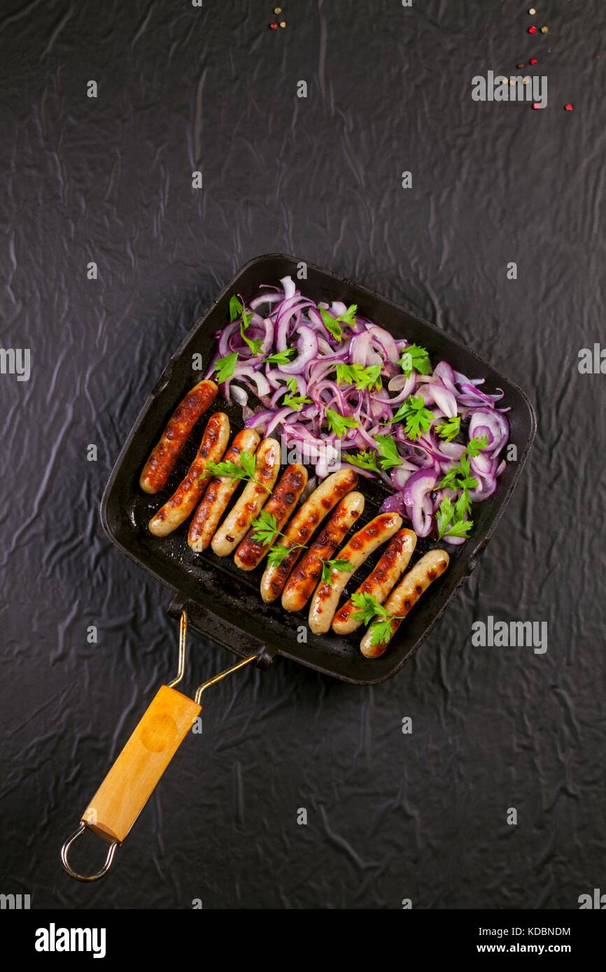 Fried sausages with parsley and onion in a pan on black background Stock Photo