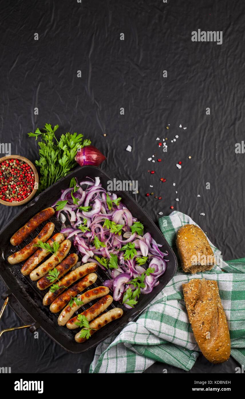 Fried sausages with parsley and onion in a pan on black background Stock Photo