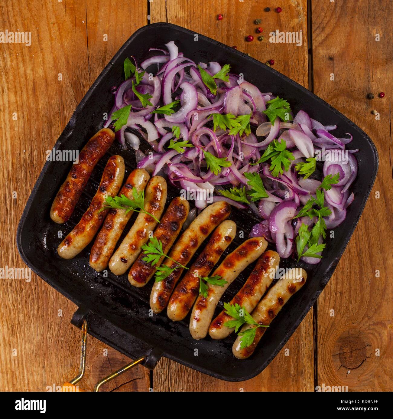 Fried sausages with parsley and onion in a pan on wooden background Stock Photo