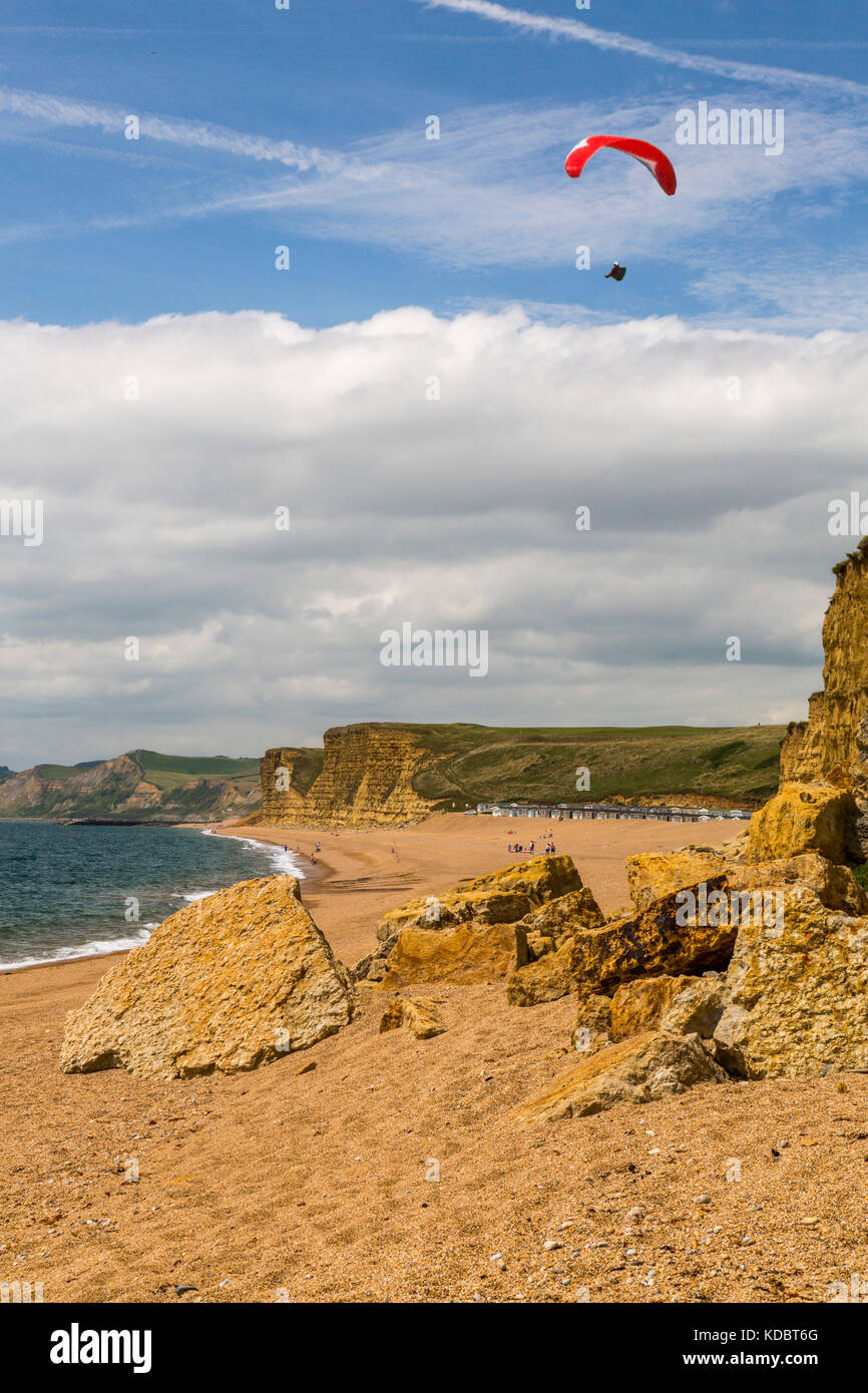 A solitary paraglider soaring above the cliffs at Burton Bradstock on the Jurassic Coast, Dorset, England, UK Stock Photo