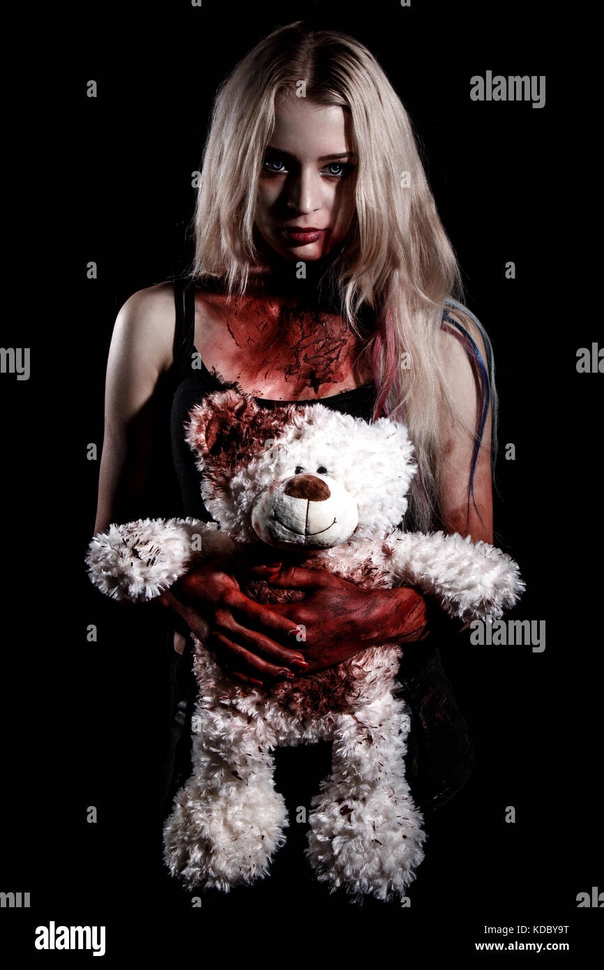 Bloody young woman holding a teddy bear over black background Stock Photo