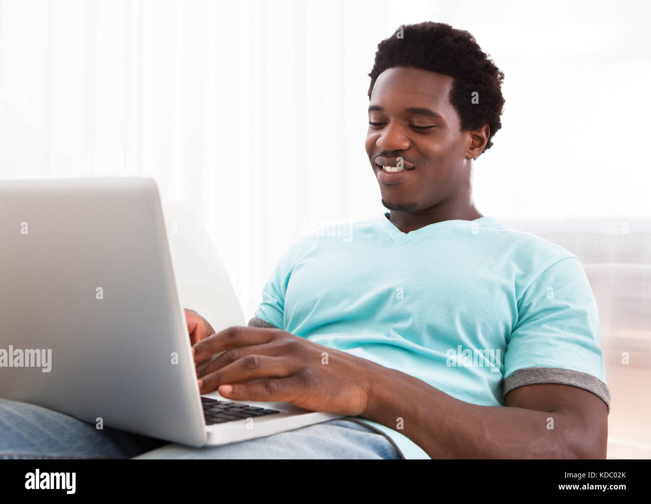 Happy Young African Man Using Laptop Sitting On Couch At Home Stock Photo