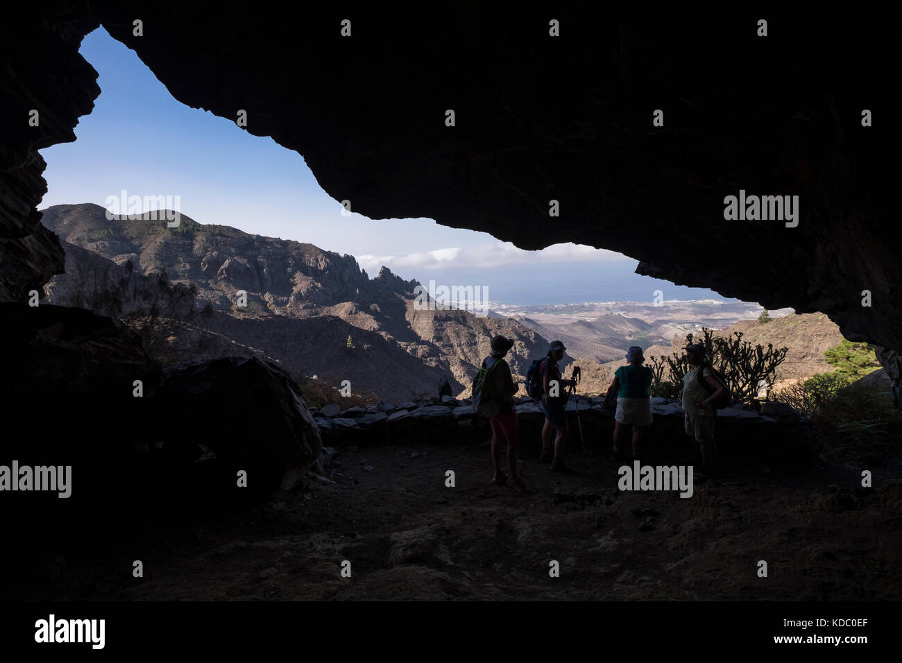 Walkers in a cave overlooking the Barranco de Los Fuentes down to the coast at Adeje, Tenerife, Canary Islands, Spain Stock Photo