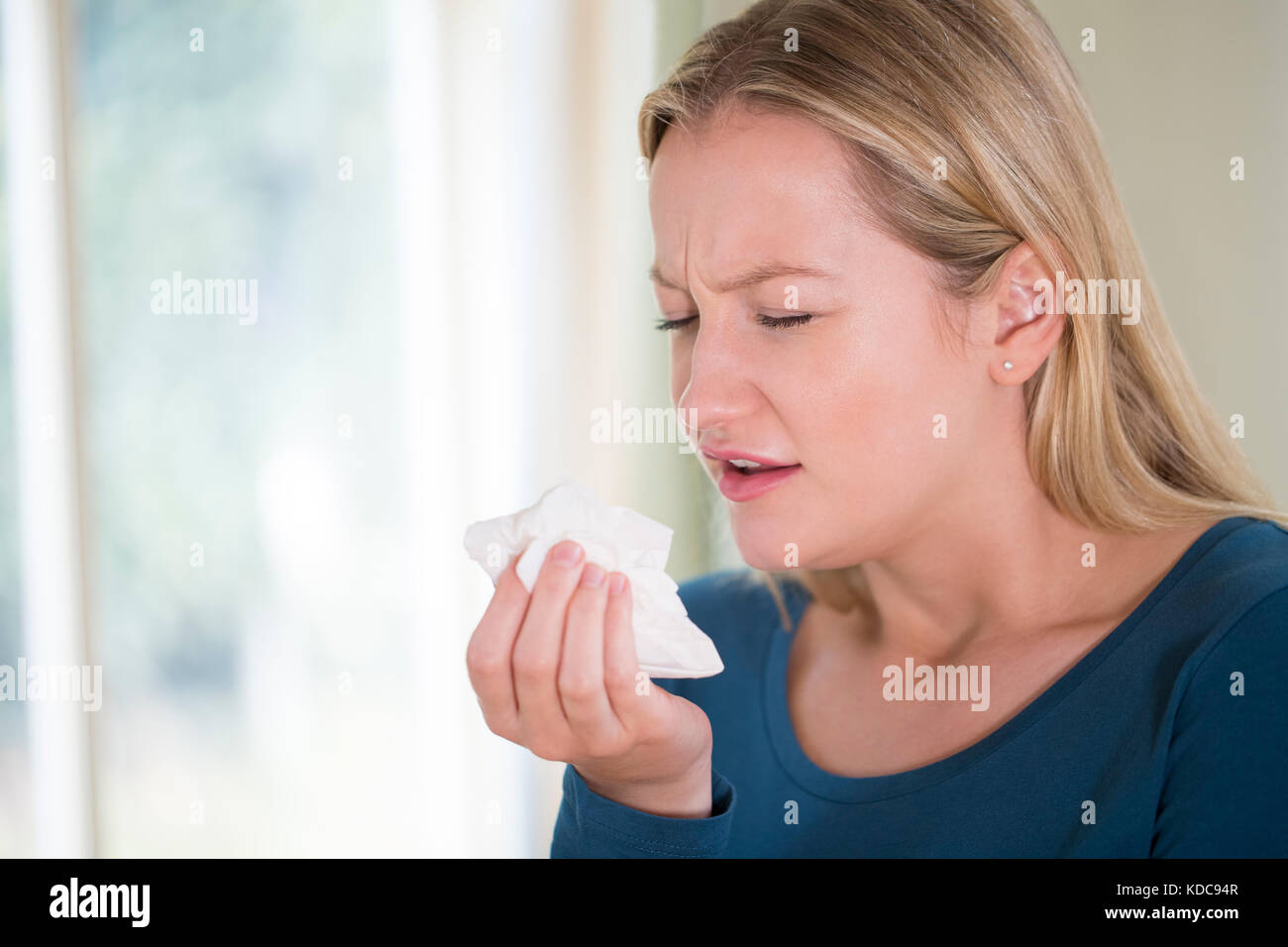Young Woman Suffering With Cold Sneezing Into Tissue Stock Photo