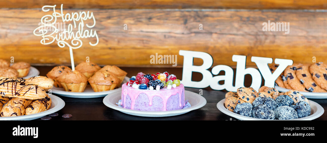 Birthday cakes and muffins with wooden greeting signs on rustic background. Wooden sing with letters Happy Birthday, Baby and holiday sweets. Stock Photo