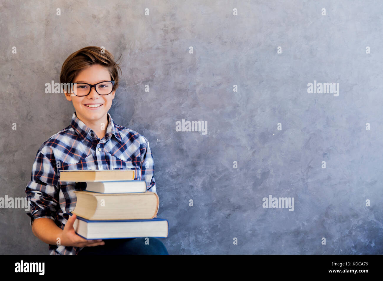 Cute teenage school boy holding books against wall Stock Photo - Alamy