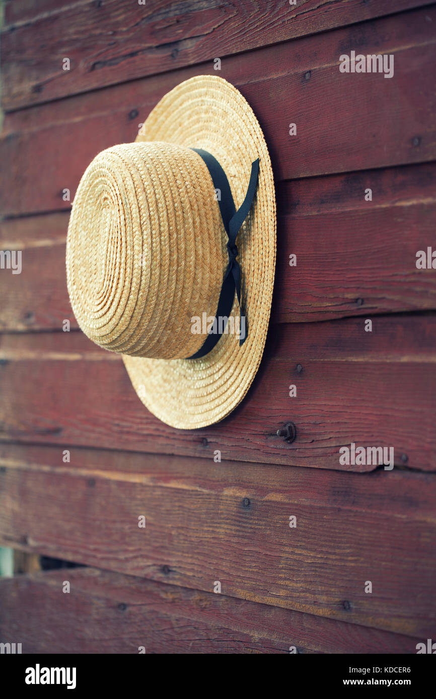 Selective focus of Amish man's straw hat hanging on a wooden barn door Stock Photo