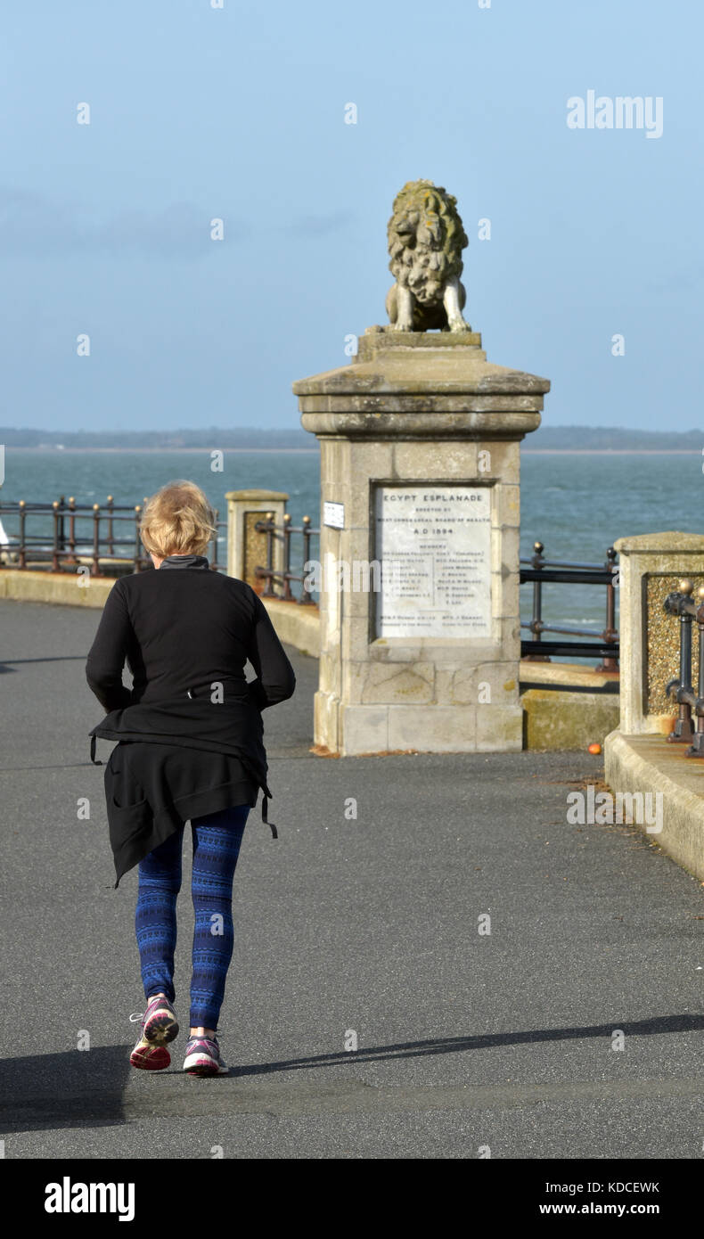 An older retired woman or pensioner jogging or running alon the seafront in an attempt to keep fit and healthy in old age or as an elderly person. Stock Photo