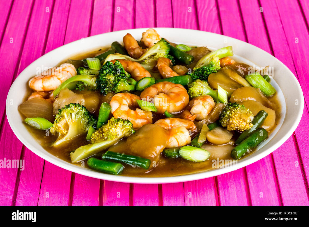 Chinese Style Stir Fried King Prawn With Ginger and Spring Onions On A Pink Wooden Background