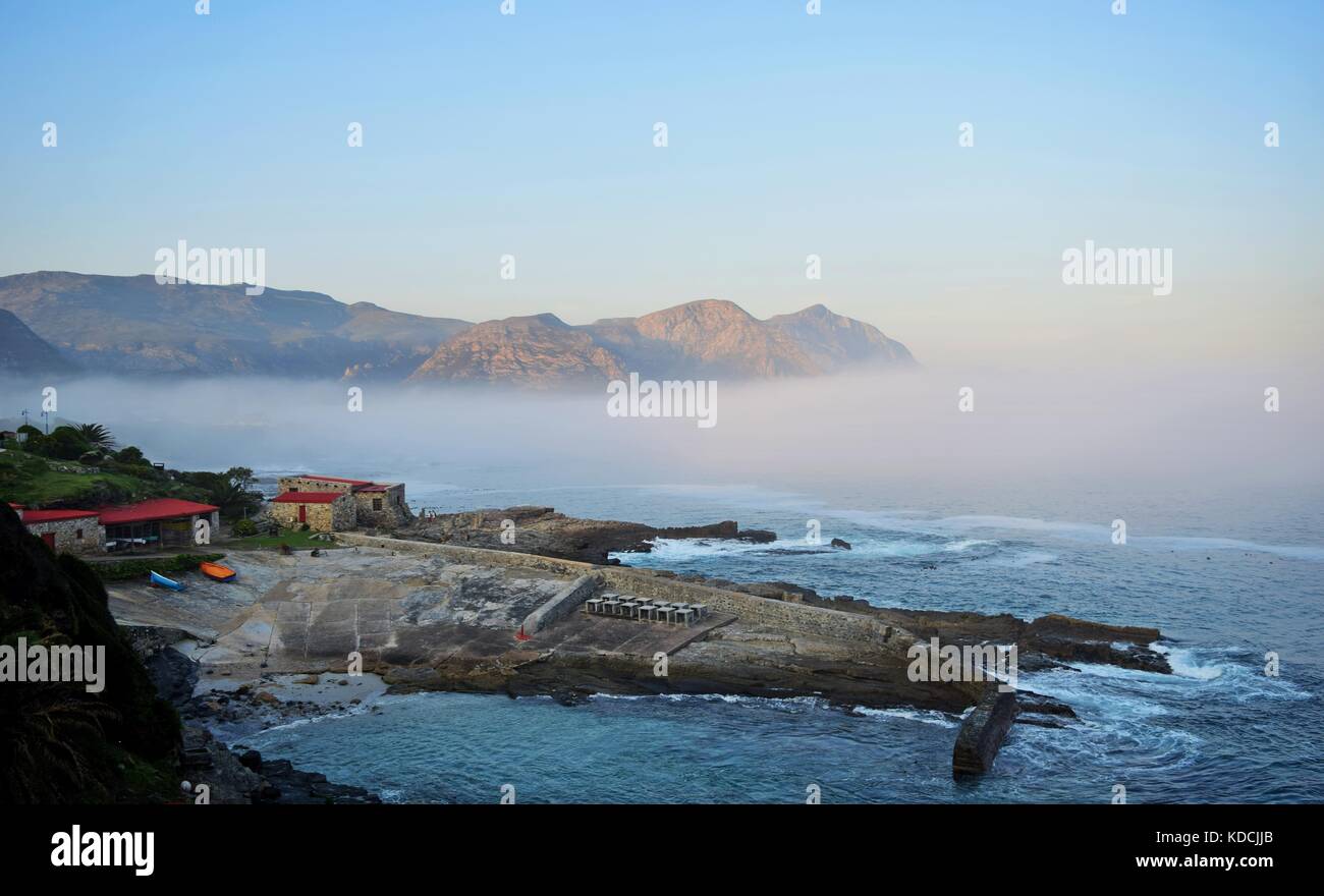 The seaside village of Hermanus along the Garden Route of Sotuh Africa. Sea mist, clouds mountains floating. Calming paradise, jetty slipway boathouse Stock Photo