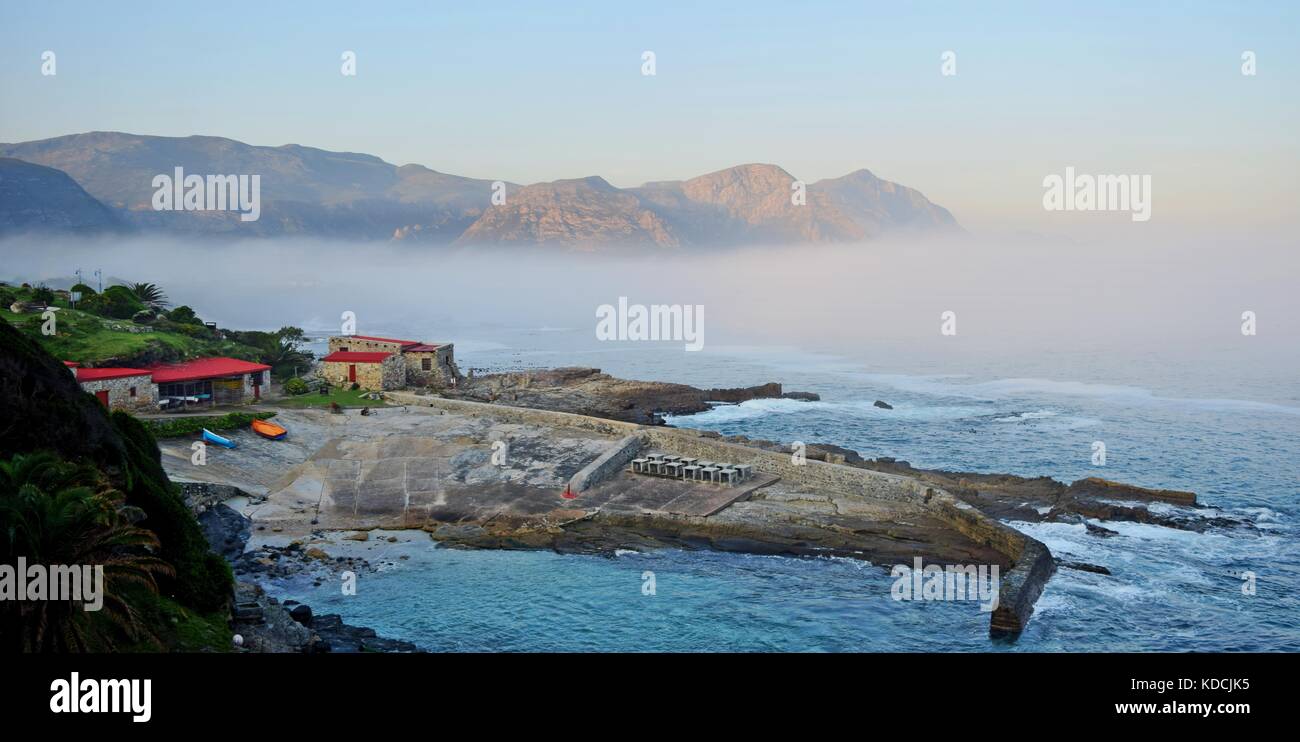 The seaside village of Hermanus along the Garden Route of Sotuh Africa. Sea mist, clouds mountains floating. Calming paradise, jetty slipway boathouse Stock Photo
