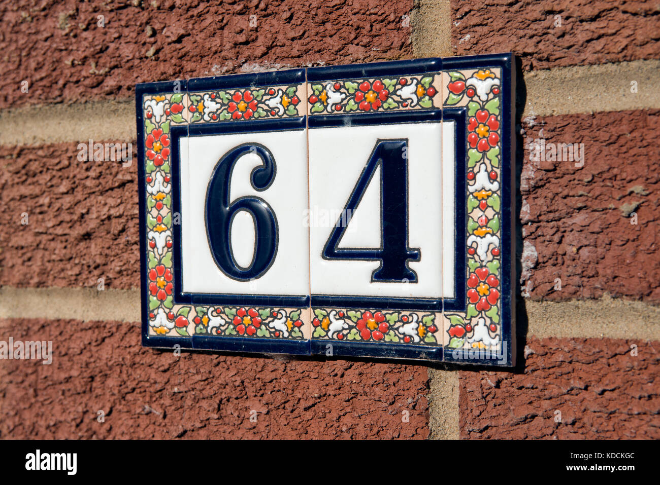 The number sixty four constructed from decorative ceramic tiles, attached to a red brick wall. Signifying the address of a UK home. Stock Photo