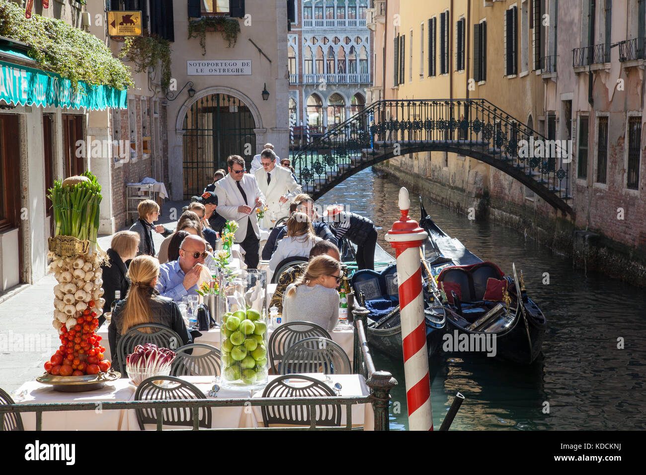 Tourists dining at the popular outdoor  Ristorante da Raffaele, San Marco, Venice, Italy alongside a canal with gondolas and gondolier in spring sunsh Stock Photo