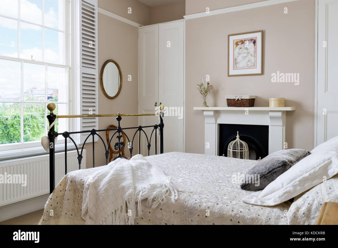 A renovated Victorian bedroom showing a shuttered window, a  fireplace and double bed with iron beadstead. Stock Photo