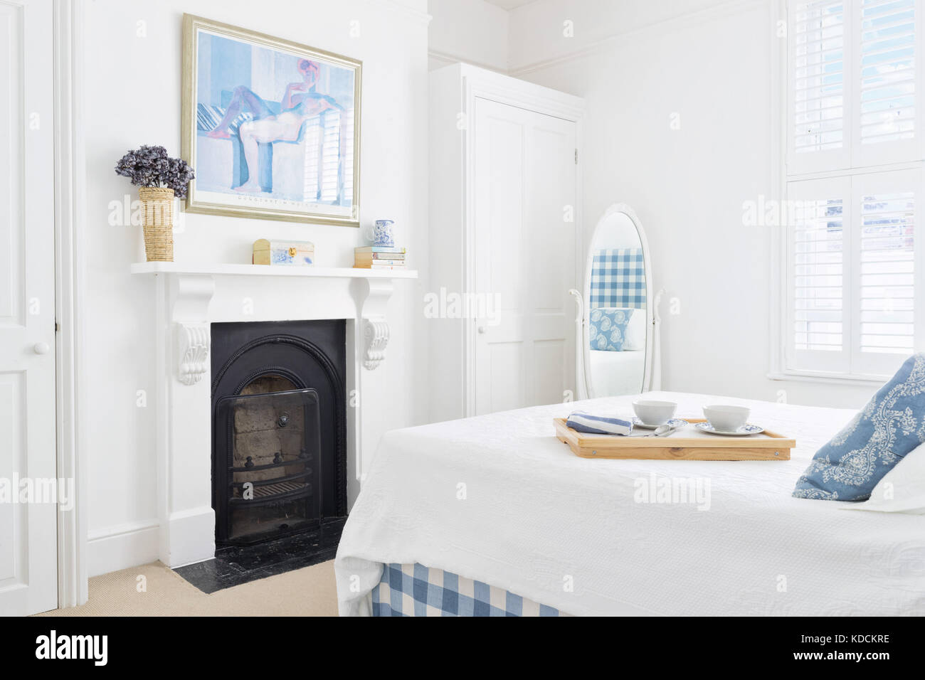A bright fresh renovated Victorian bedroom showing a shuttered window, a cast iron fireplace and double bed with a breakfast tray placed upon it. Stock Photo