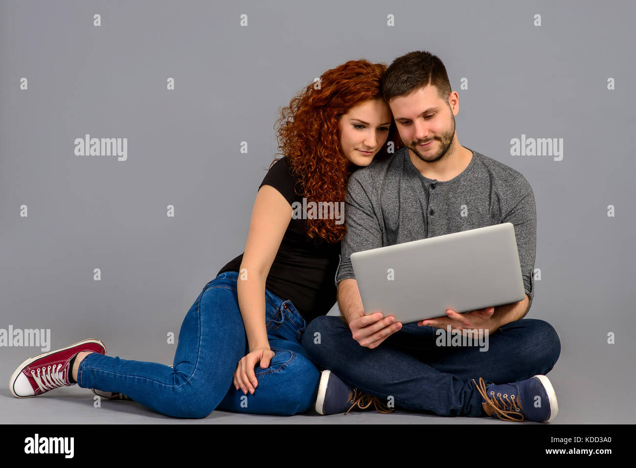 A beautiful young couple sitting on the ground and looking at a laptop ...