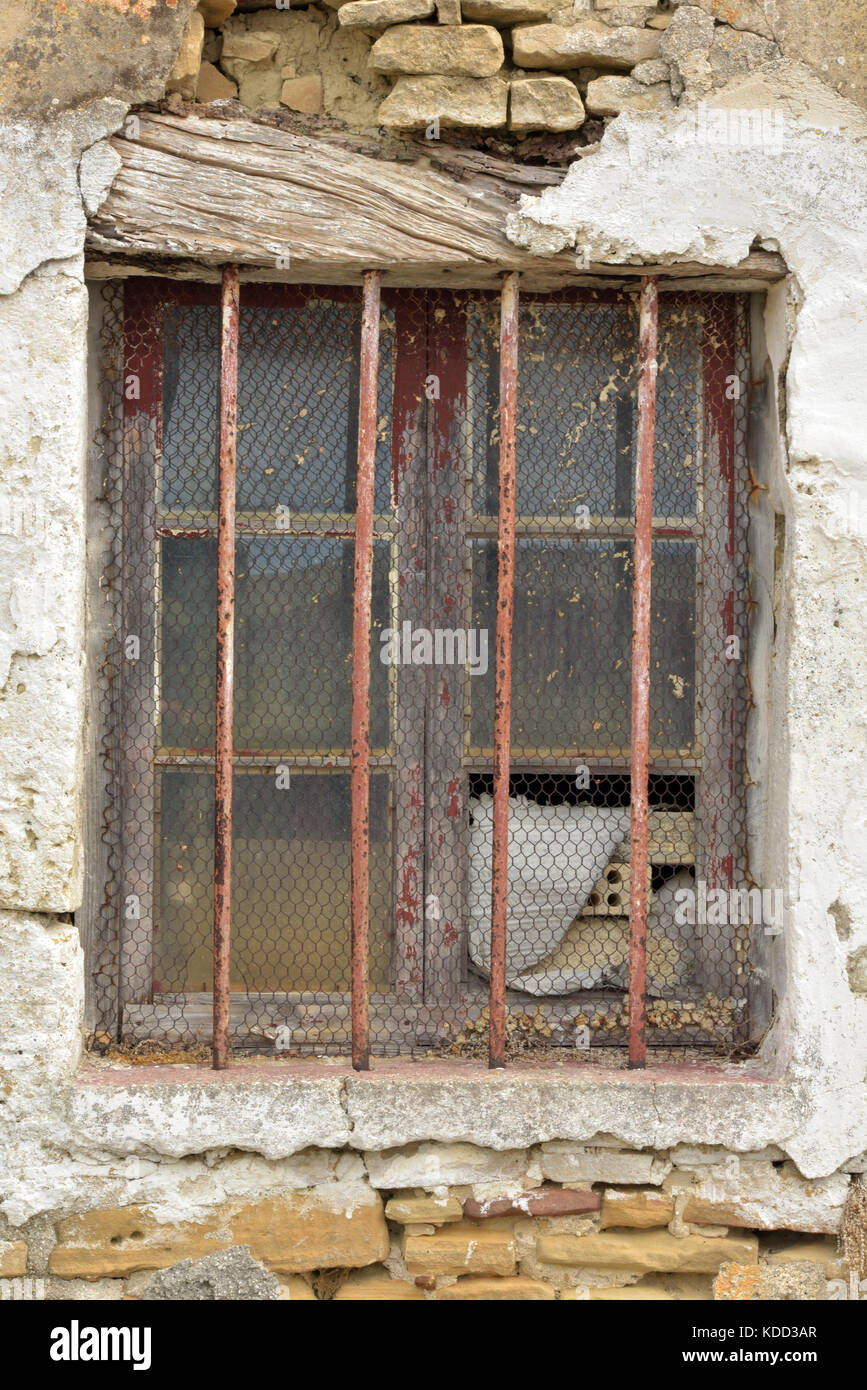 a barred window with cracked plaster and broken glass showing neglect ...