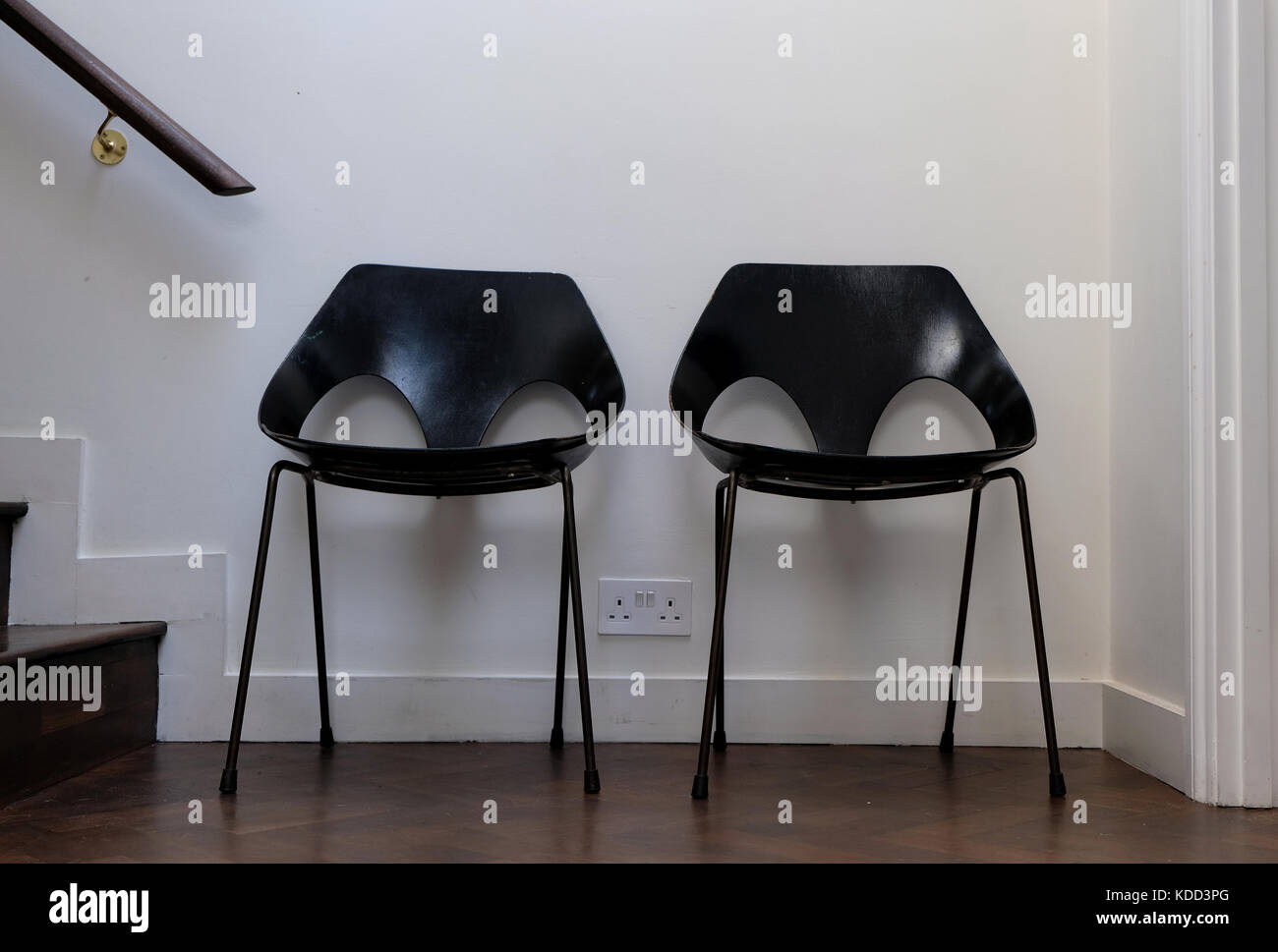 Two black retro chairs standing against a white wall, with dark wooden