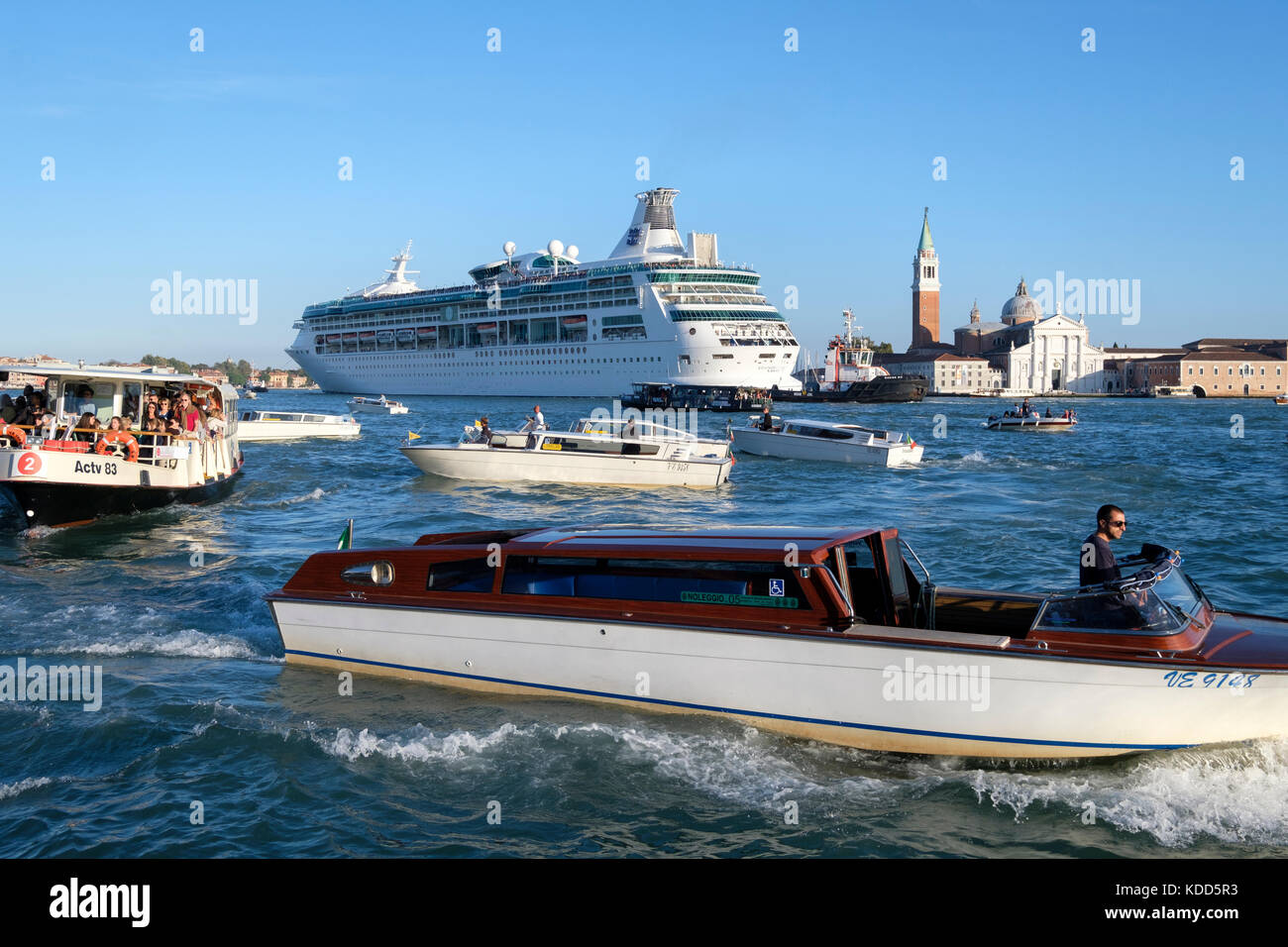 Congestion in the Venetian lagoon as the the Royal Caribbean Cruise ship, 'Rhapsody of the Seas' makes its way past San Giorgio Maggiore. Venice, Ital Stock Photo