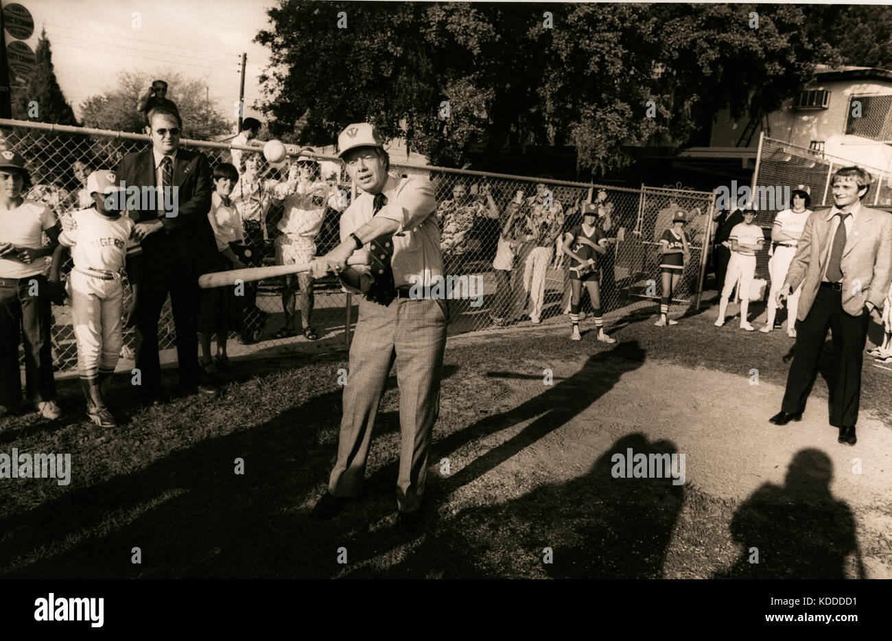 White House press secretary Jody Powell (right) watches as the president takes a swing on a middle school baseball field. A Secret Service agent holds Stock Photo