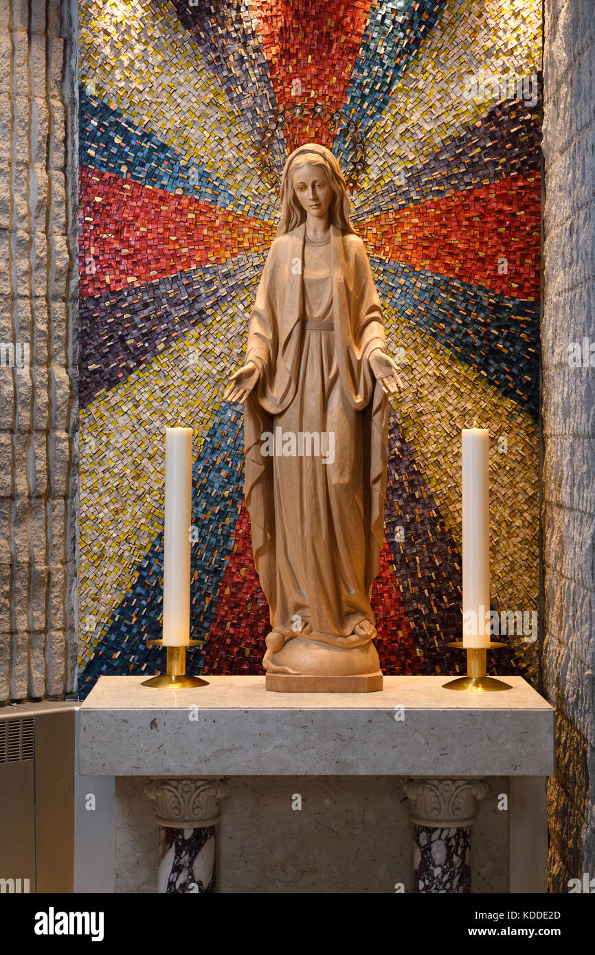 Wood carved statue of Mary Mother of God with 12 star crown standing on moon and serpent at side altar with candles in a Roman Catholic church Stock Photo