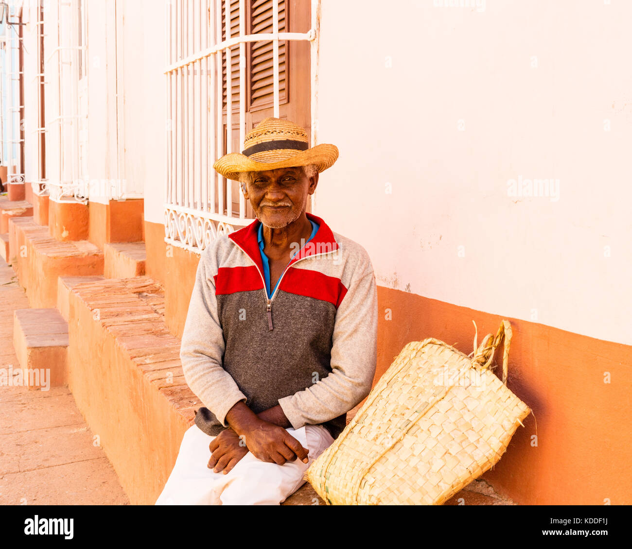 Smiling local Cuban man with hat sitting outside a house watching the ...