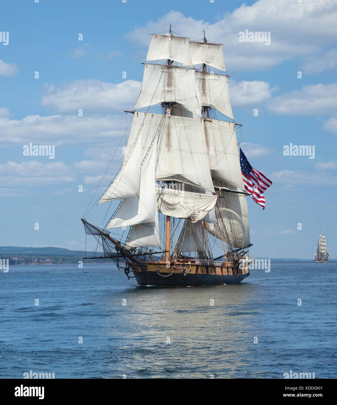 A tall ship known as a brigantine sails on blue water with an American flag flying Stock Photo