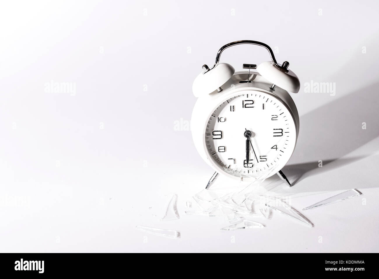 White crashed alarm clock and shards of glass on white background. Stock Photo