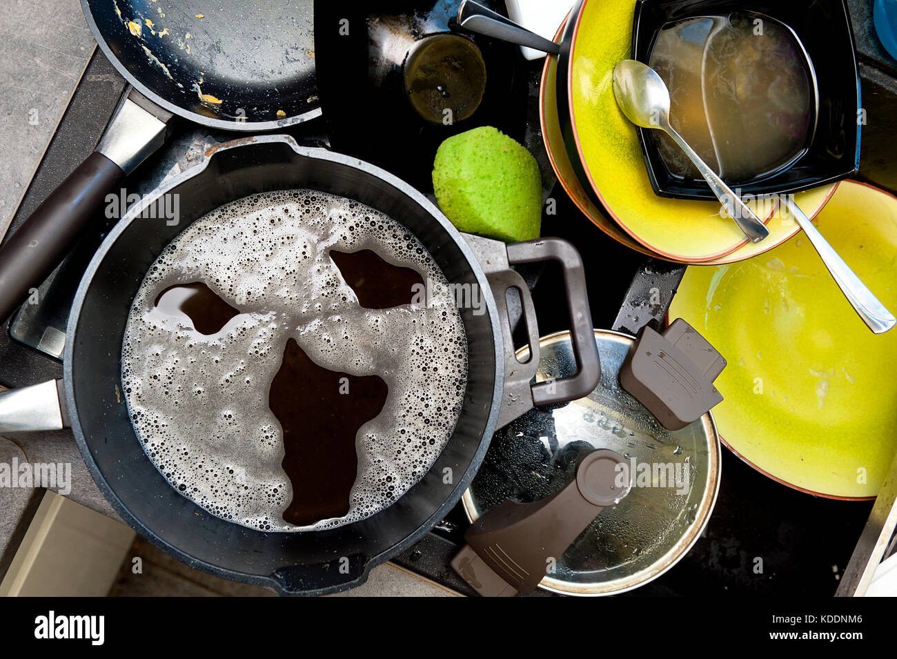 A pile of dirty dishes in the sink and screaming face made of soap foam Stock Photo