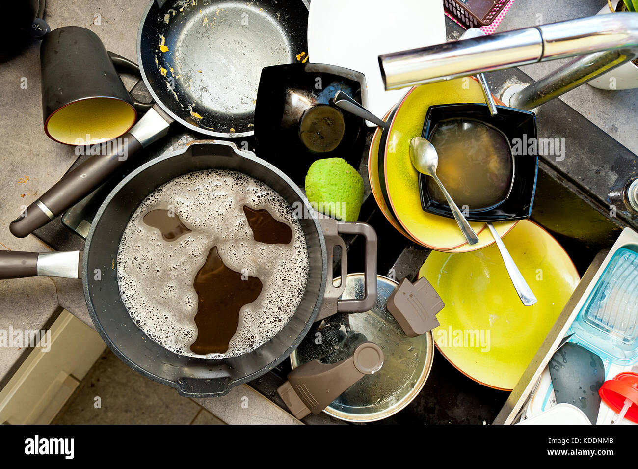 A pile of dirty dishes in the sink and screaming face made of soap foam Stock Photo