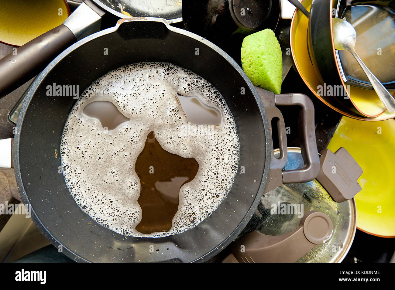 A pile of dirty dishes in the sink and screaming face made of soap foam Stock Photo