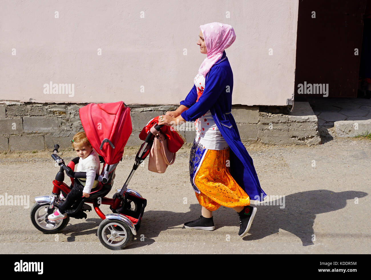 Woman strolling baby in Muslim village of       Woman strolling with child in Muslim village of Ribnovo, Bulgaria. Stock Photo