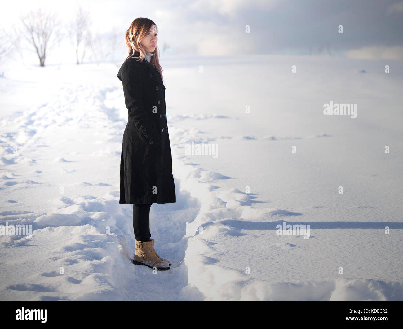 Asian girl with black coat at Mild Seven Hills, Biei, Hokkaido, Japan, in winter, standing and gazing afar Stock Photo