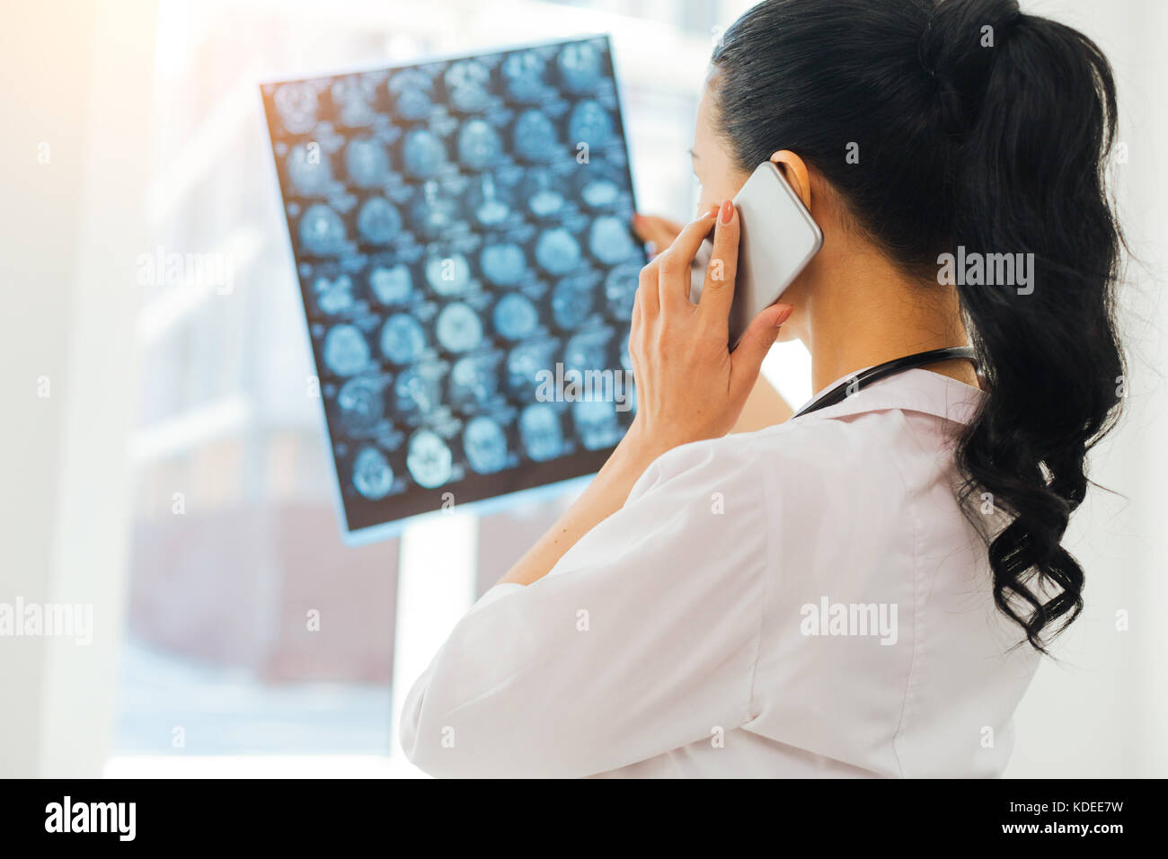 Female radiologist examining MRI scan during phone talk at work Stock Photo