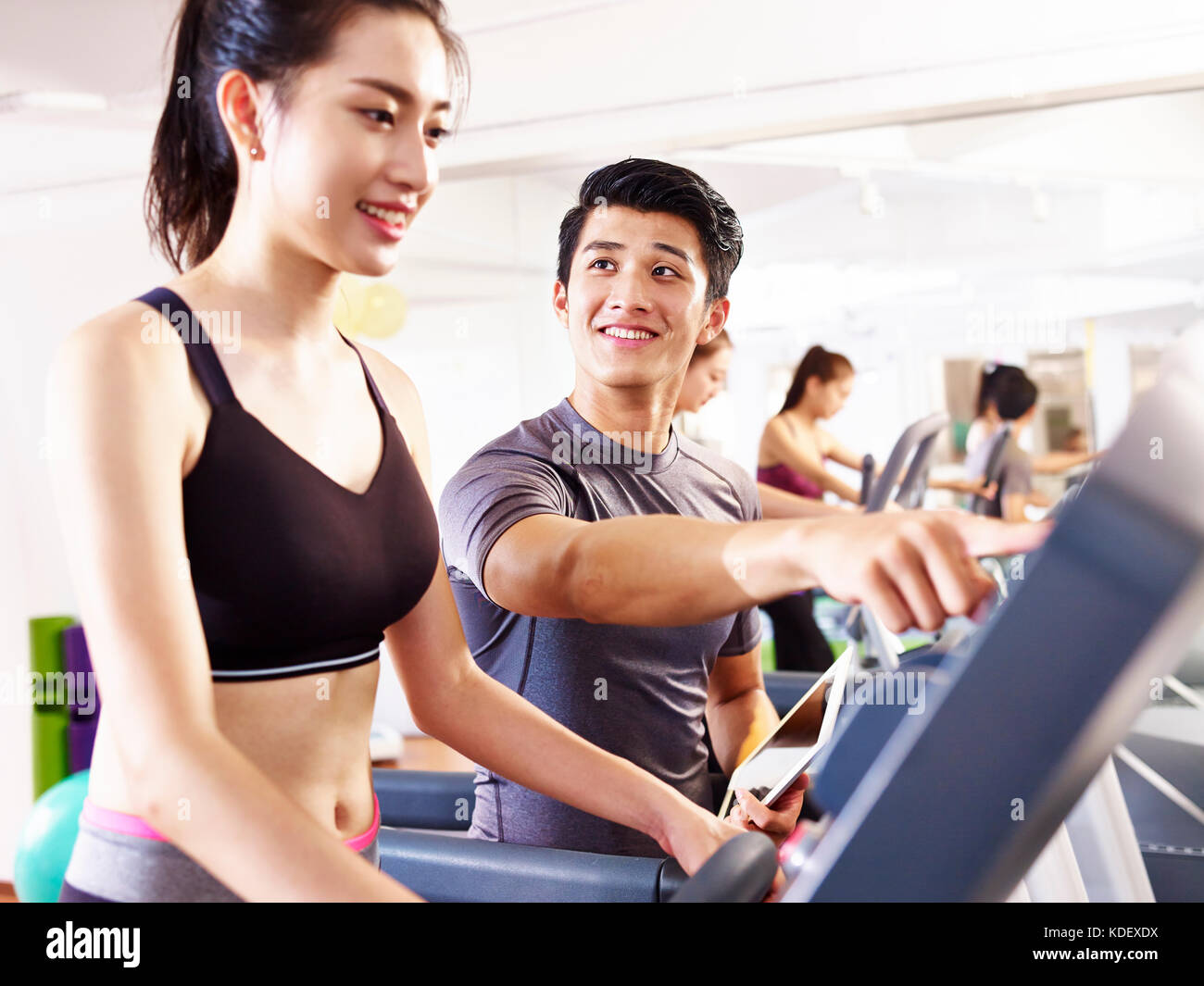 young asian woman running on treadmill coached by young trainer. Stock Photo