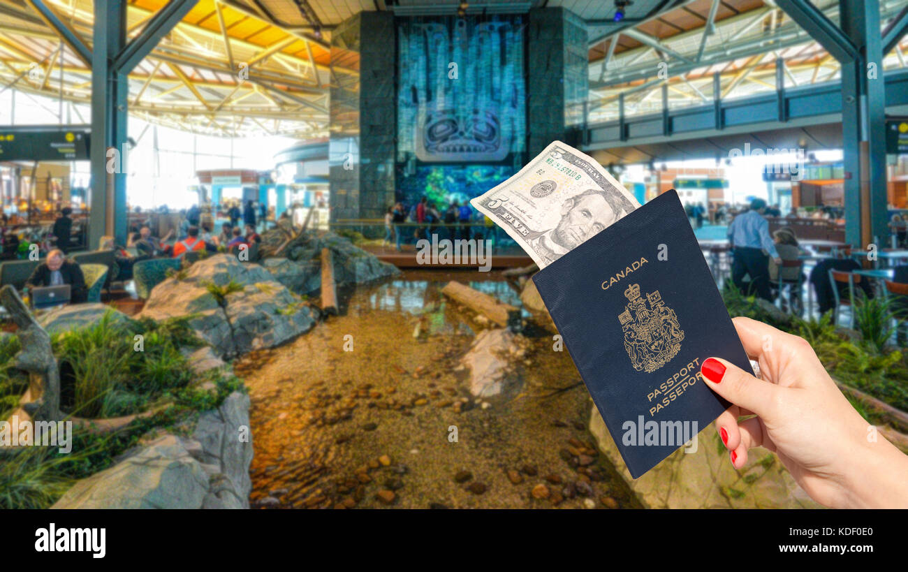 Vancouver International Airport - 11 April, 2017: Hand holding a Canadian passport with a $5 note at Vancouver International Airport lounge. Stock Photo