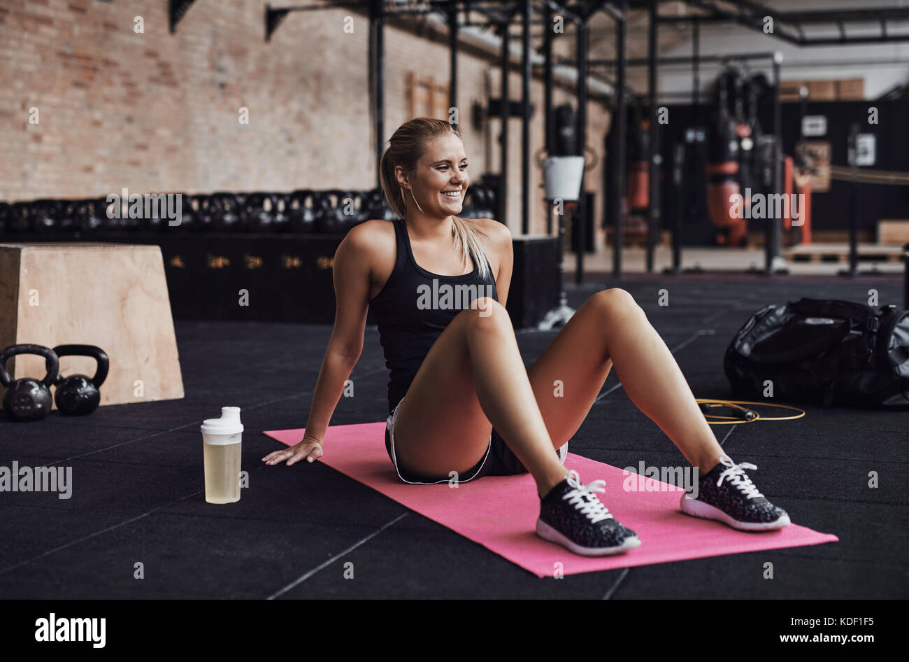 Fit young blonde woman in sportswear sitting on an exercise mat and ...