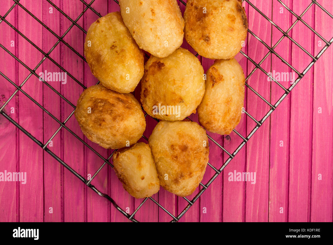 Roast Potatoes on a Steel Kitchen Cooling Rack Against a Pink Wooden